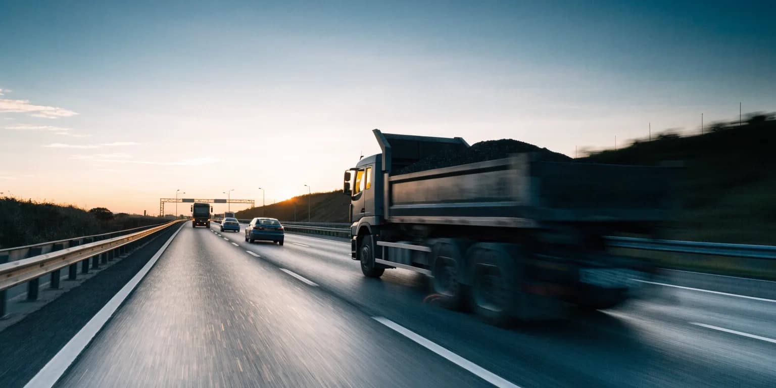 A tipper on an almost empty motorway at first light, headlights on under a pale sky
