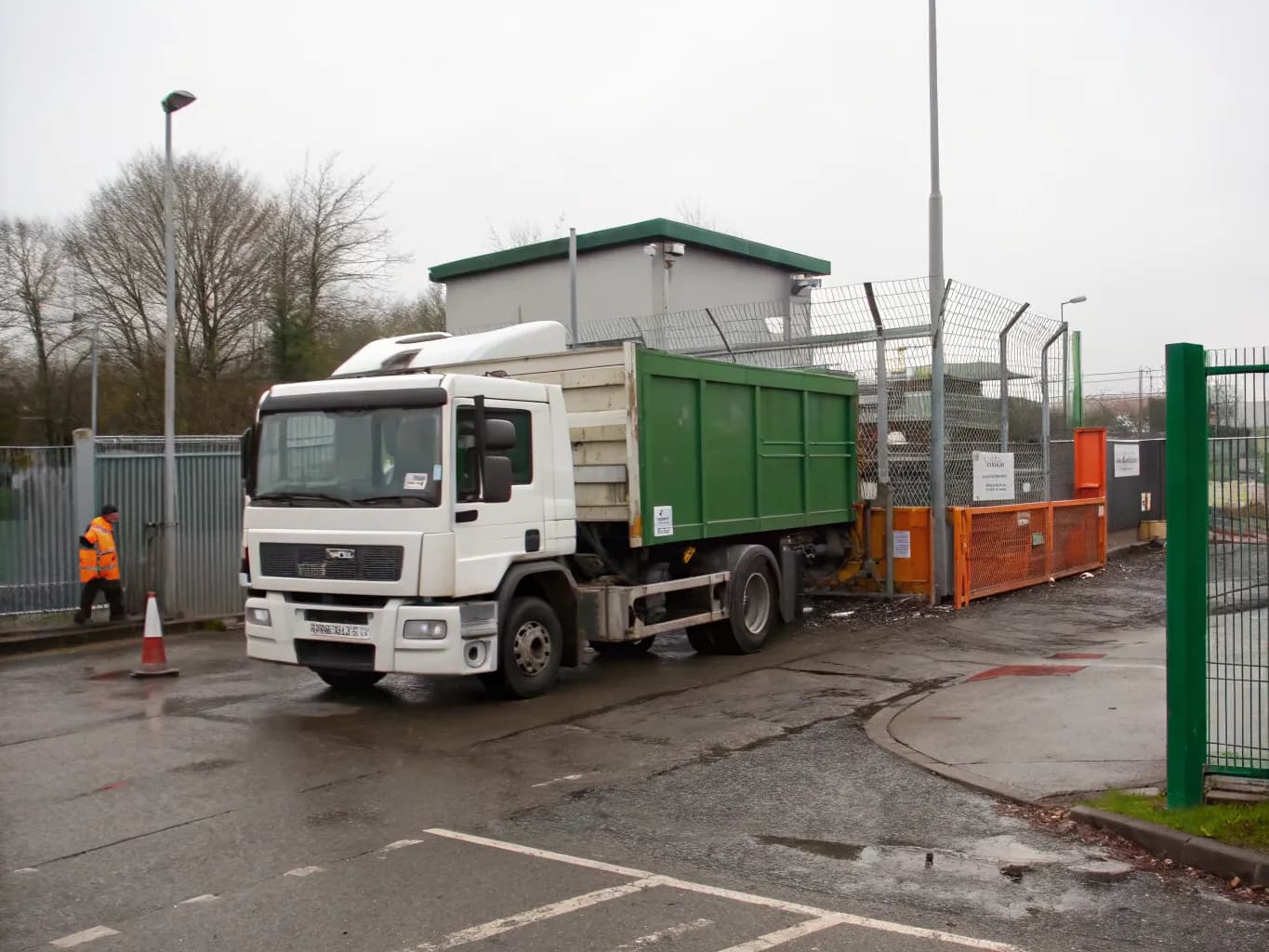 Tipper lorry arriving at the gatehouse of a waste recycling facility with an operative on duty at the fence