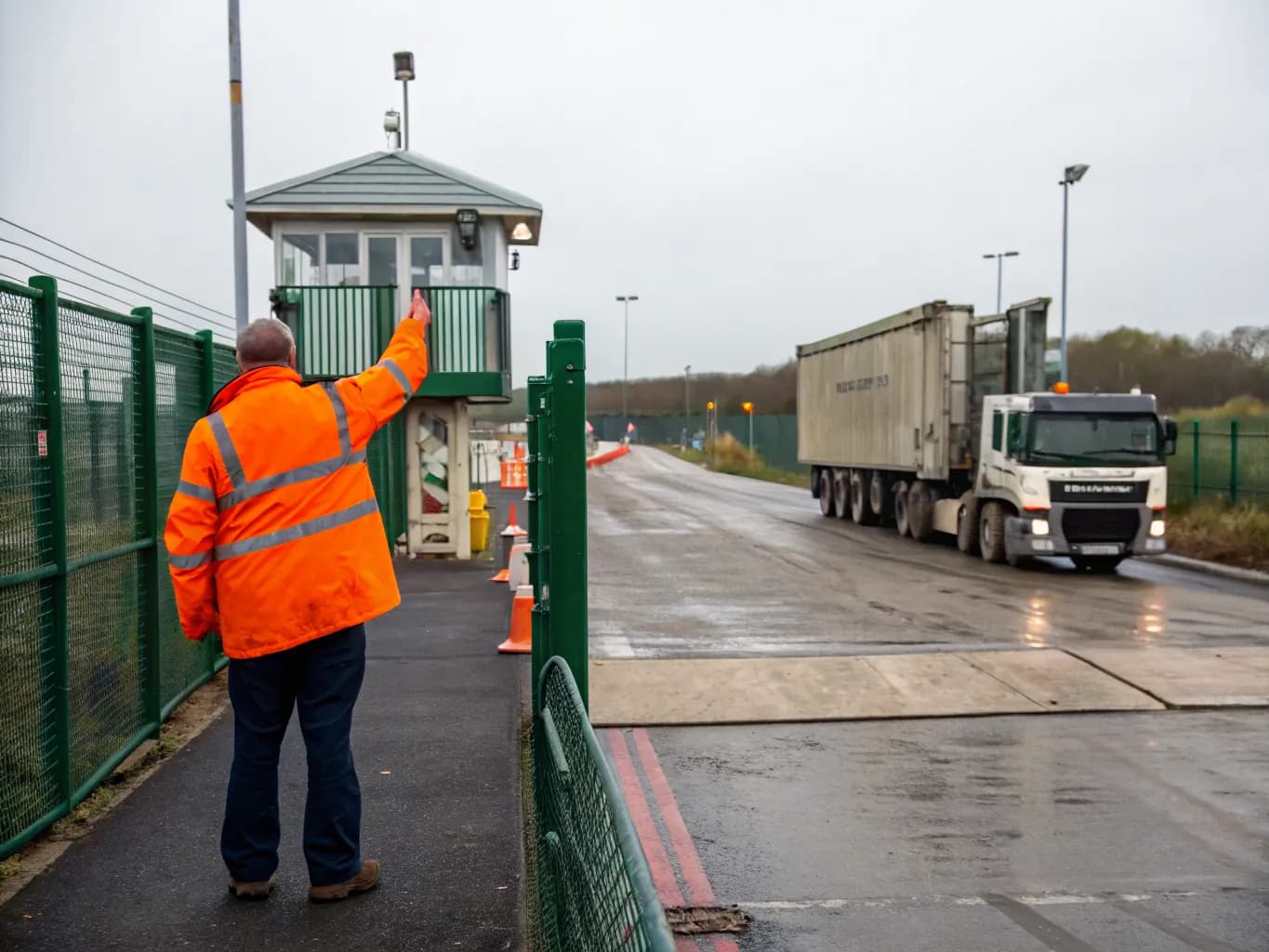 Site operative in orange hi-vis waving a tipper lorry over the weighbridge at a waste transfer station gate