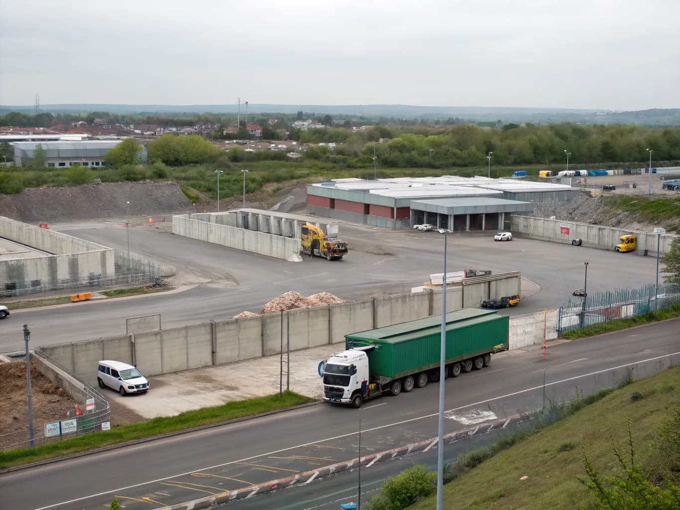 A wide view over a large waste transfer station estate with concrete bays, moving vehicles and depot buildings.