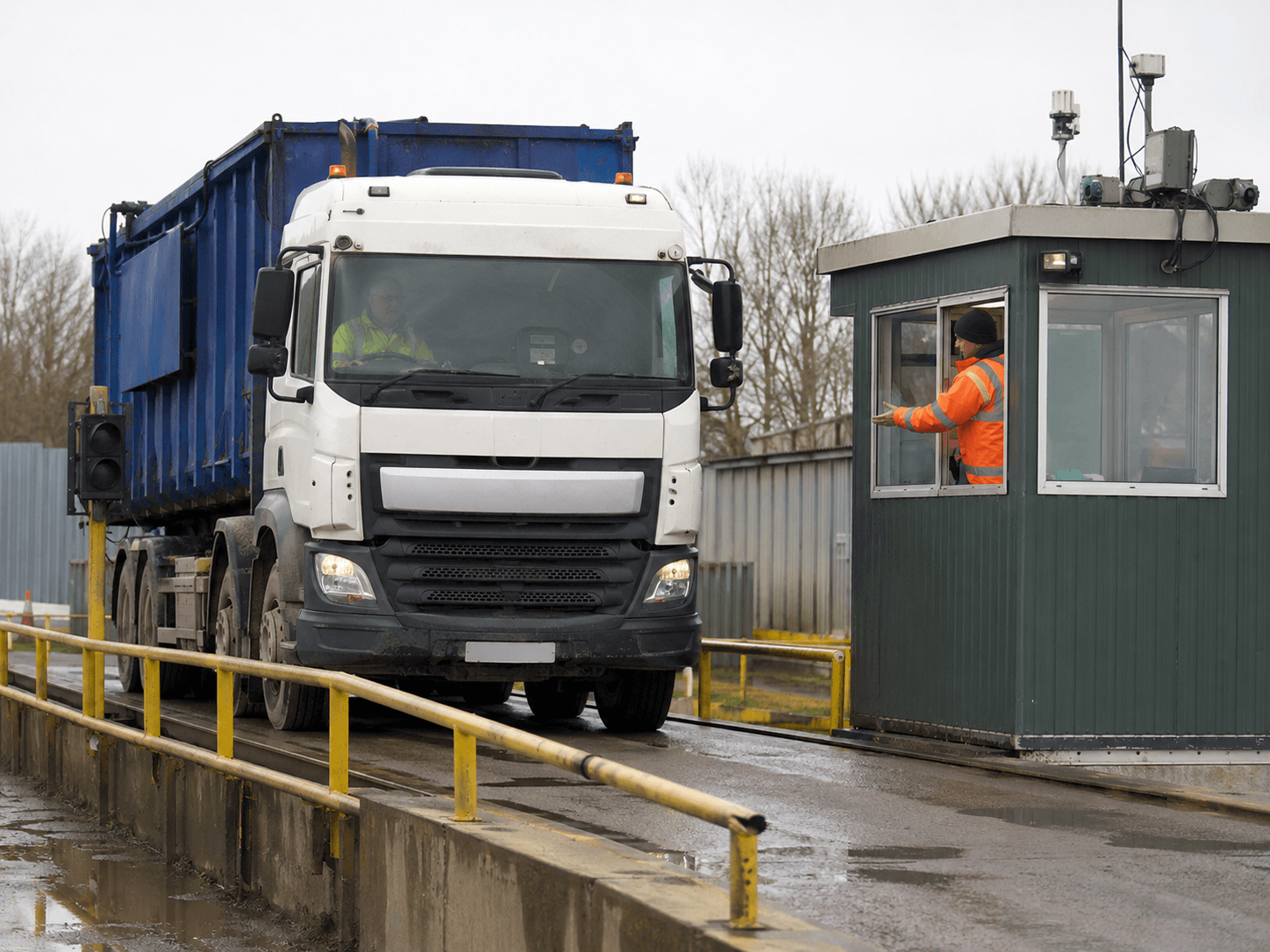 A tipper lorry on a weighbridge at a UK waste transfer station, the gate operative checking a tablet as the load is recorded