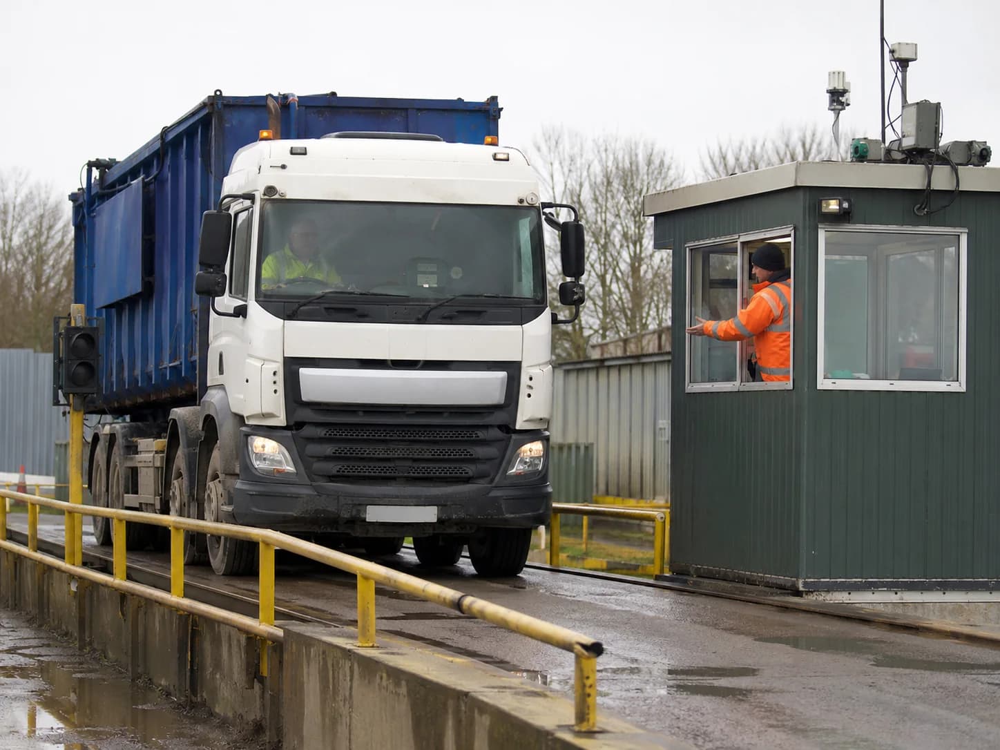 A tipper lorry on a weighbridge at a UK waste transfer station, the gate operative checking a tablet as the load is recorded